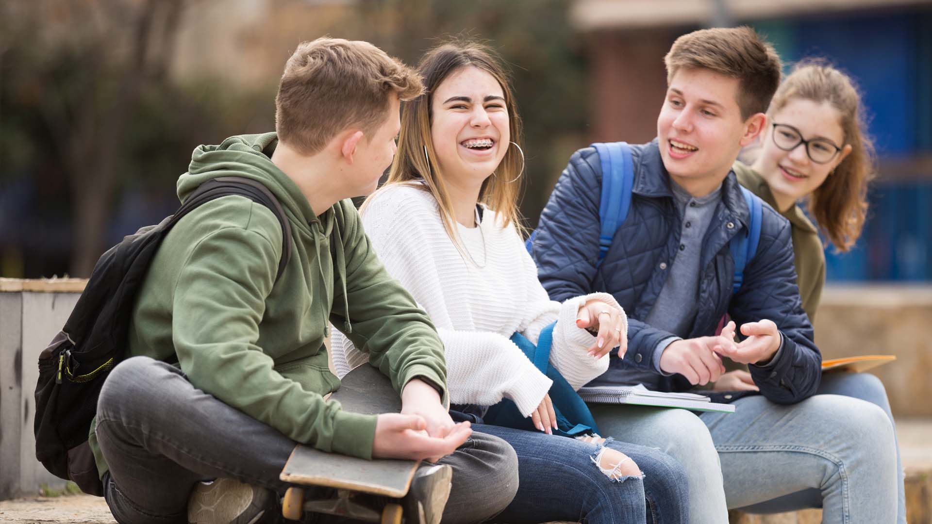 En gruppe teenagere sidder og taler og griner sammen. FOTO: AdobeStock