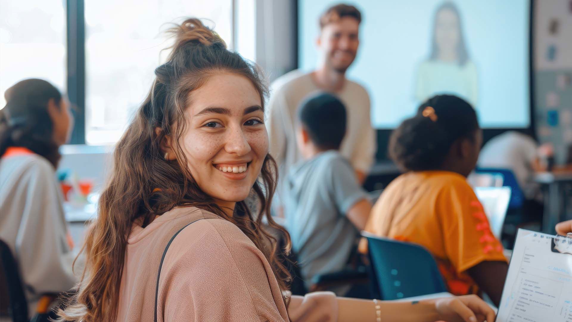 Ung kvinde smiler mens hun sidder i klasselokalet. FOTO: AdobeStock